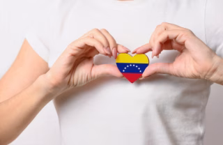 Person making a heart with his hand, holding a wooden heart with the Venezuelan flag.