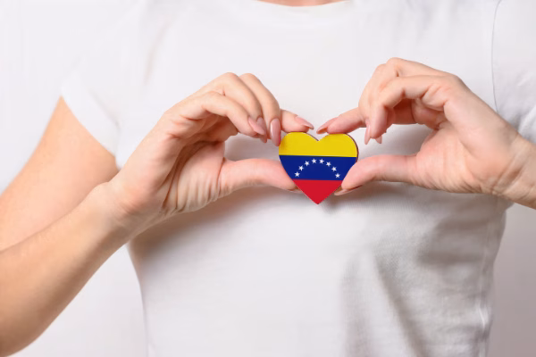 Person making a heart with his hand, holding a wooden heart with the Venezuelan flag.