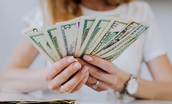 young woman's hands holding a lot of dollar bills